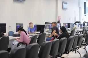 Ambiente interno da Casa do Trabalhador de Curitiba. Em primeiro plano, pessoas aguardam nas cadeiras de espera. Ao fundo, cidadãos recebem atendimento presencial de funcionários nos guichês com divisórias transparentes.